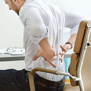 sedie ergonomiche, uomo con dolore alla schiena seduto con mal di schiena